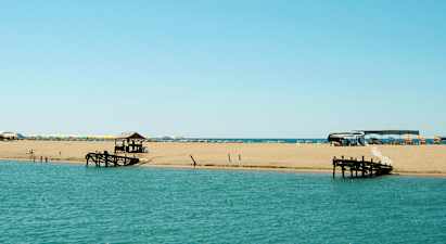 En strand ved havet med liggestole og parasoller samt en træbro. (AI-genereret tekst)