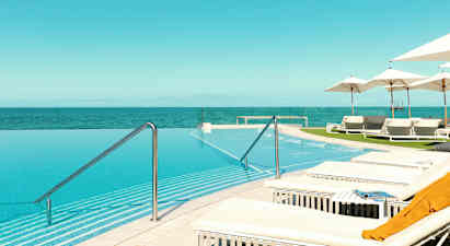 En infinitypool med udsigt over havet, omgivet af liggestole og parasoller. (AI-genereret tekst)