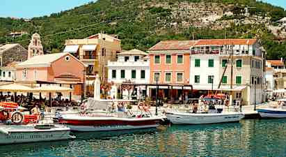 En havn med flere både foran farverige bygninger og omgivet af bakker. (AI-genereret tekst)