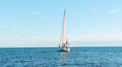 En sejlbåd sejler på et åbent hav under en klar himmel. (AI-genereret tekst)