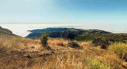 Solrig bjergudsigt med skyet panorama og tør vegetation. (AI-genereret tekst)