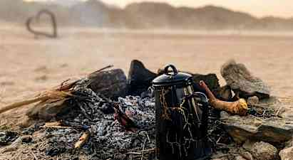En kaffekande står ved et udbrændt bål i et ørkenlandskab. (AI-genereret tekst)
