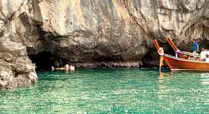 Personer svømmer i vandet ved en klippe, og to træfartøjer flyder tæt på. (AI-genereret tekst)
