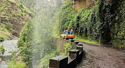 En gul-orange jeep på en vej ved et vandfald i en grøn dal. (AI-genereret tekst)