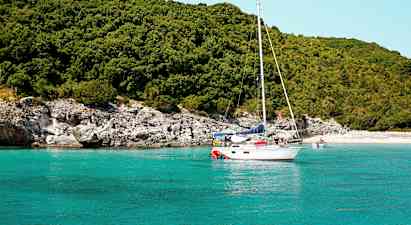 Sejlbåd på turkis vand nær en frodig kyst. (AI-genereret tekst)