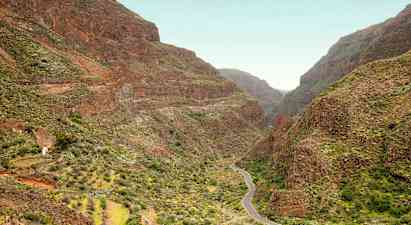 En smal vej snoer sig gennem en dal omgivet af stejle bjerge med grøn vegetation. (AI-genereret tekst)