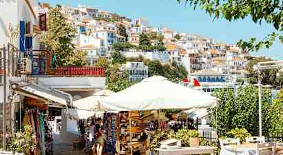 En malerisk by med hvide huse med røde tage på en skråning, parasoller og salgsboder i forgrunden. (AI-genereret tekst)