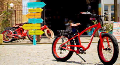 Rød cykel på brostensbelægning med farverige vejskilte i baggrunden. (AI-genereret tekst)