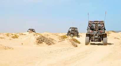 Tre firehjulere kører gennem sandklitter i en ørken. (AI-genereret tekst)