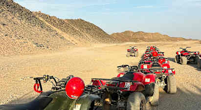 En række firehjulede ATV'er er parkeret på en ørkenvej omgivet af sandede bakker. (AI-genereret tekst)