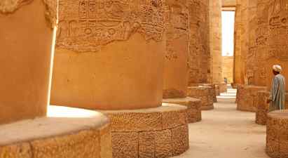 Stensøjler med hieroglyffer i en historisk bygning, en person står tæt på. (AI-genereret tekst)