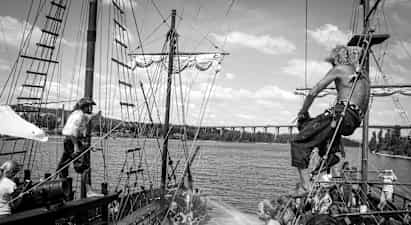 En scene på et gammeldags piratskib med personer, der interagerer og vandspredning mellem skibene. (AI-genereret tekst)