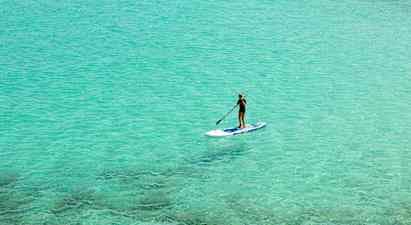 Person der padler stående på et paddleboard i klart turkisblåt vand. (AI-genereret tekst)