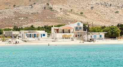 Billede af en klarblå havbugt med en sandstrand samt huse og bakker i baggrunden. (AI-genereret tekst)