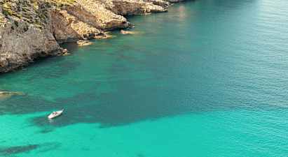 En båd ligger forankret i klart turkis vand nær en klippekyst. (AI-genereret tekst)