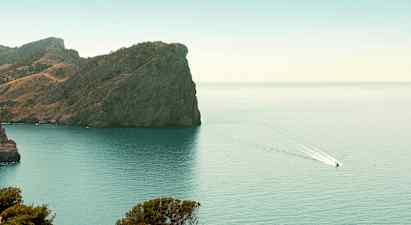 En klippe ved en kyst med en båd, der sejler på vandet. (AI-genereret tekst)