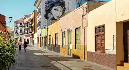 Farverige husfacader langs en gangsti med to personer der går. (AI-genereret tekst)