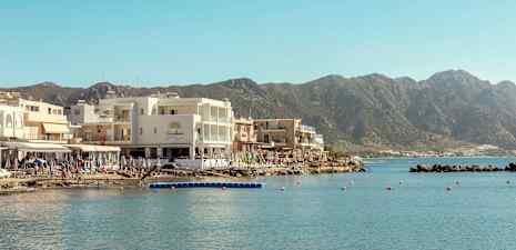 Udsigt over huse ved vandet med bjerge i baggrunden. (AI-genereret tekst)