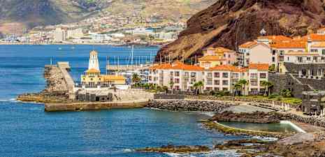 En kyst med bygninger med røde tage, en havn og bakker i baggrunden. (AI-genereret tekst)