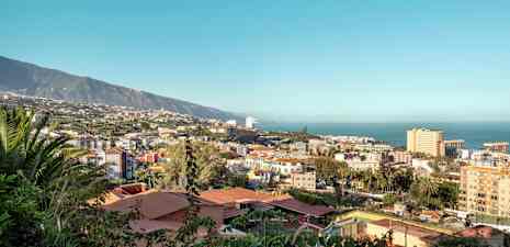 Udsigt over en by med en kyststrækning ved havet og bjerge i baggrunden. (AI-genereret tekst)