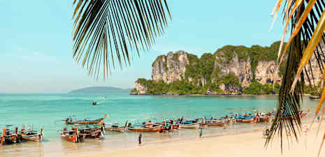 En strand med longtailbåde og klipper ved havet. (AI-genereret tekst)