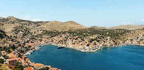 Billede af en bugt omgivet af bakker med huse og småbåde ved vandet. (AI-genereret tekst)