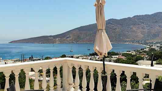 En udsigt fra en terrasse med rækværk, en parasol og havet og bjerge i baggrunden. (AI-genereret tekst)