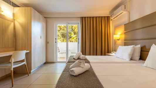 Et hotelværelse med to enkeltsenge, skrivebord og en glasdør, der fører ud til en altan. (AI-genereret tekst)