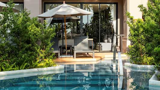 En terrasse med liggestole og parasol ved en pool, omgivet af grønne planter. (AI-genereret tekst)
