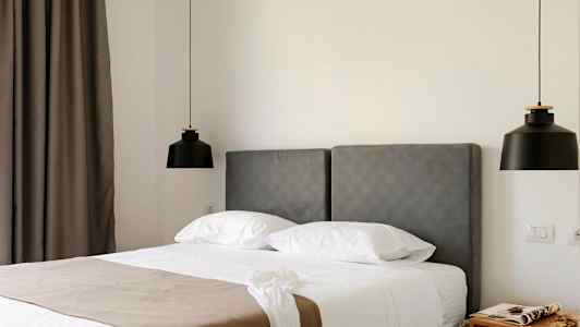 Hotelværelse med grå sengegavl, hvid seng og to sorte hængende lamper. (AI-genereret tekst)