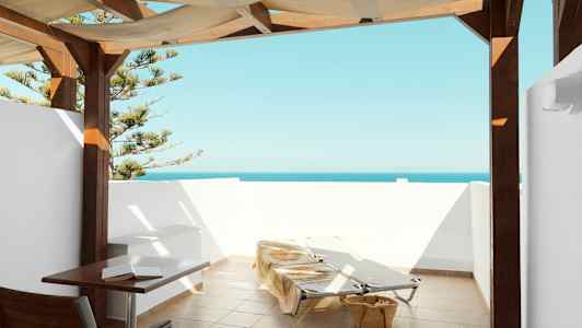 Terrasse med havudsigt, liggestole og bord under overdækning. (AI-genereret tekst)