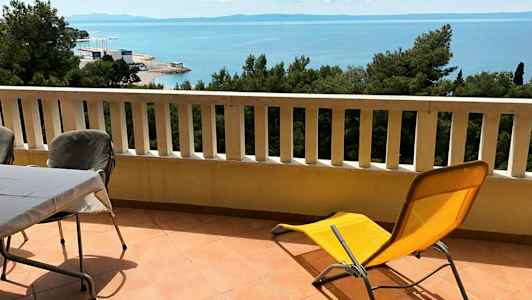 Altan med bord, stole og liggestol samt udsigt over havet. (AI-genereret tekst)