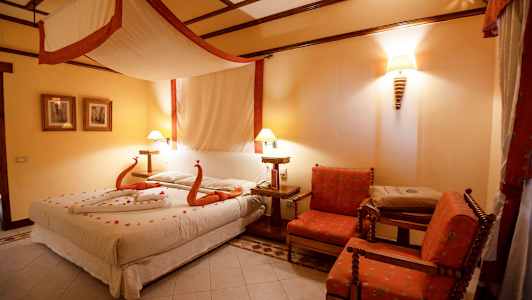 Et hotelværelse med en stor seng dekoreret med håndklæder formet som svaner og blomster, to stole og et bord. (AI-genereret tekst)