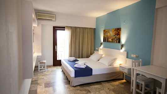 Et hotelværelse med en dobbeltseng, blå vægdekoration og et bord med stole. (AI-genereret tekst)