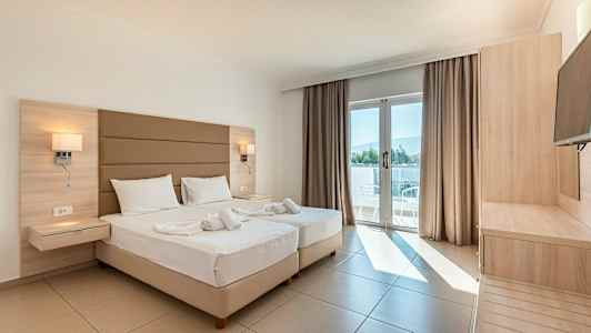 Et lyst hotelværelse med to senge, en altandør med udsigt og trætremøbler. (AI-genereret tekst)