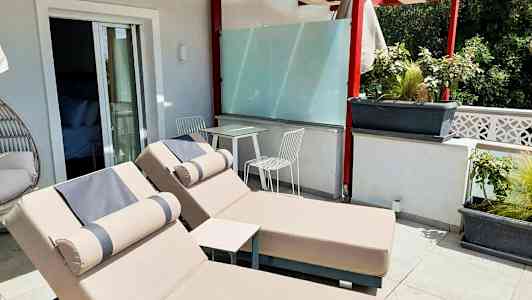 Terrasse med to solsenge og et bord med to stole under en pergola. (AI-genereret tekst)