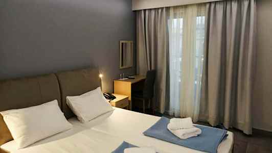 Et hotelværelse med en dobbeltseng, skrivebord og et vindue med gardiner. (AI-genereret tekst)