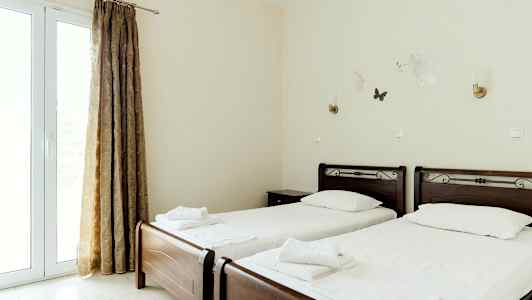 To enkeltsenge med hvide sengelinned og mørke træsengegavle, beliggende i et lyst rum med gardiner og vægdekorationer. (AI-genereret tekst)