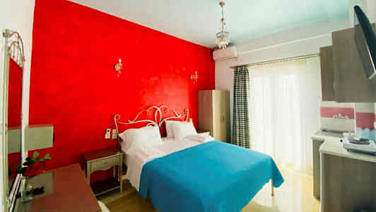 Et hotelværelse med en dobbeltseng, rødt vægparti og lyseblåt sengetæppe. (AI-genereret tekst)