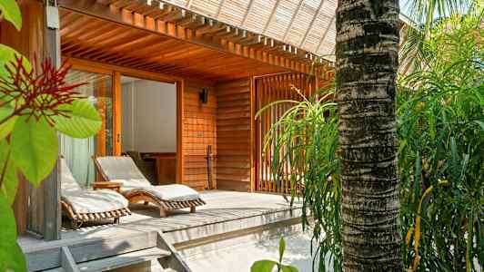 Træterrasse med solsenge og omgivelser med grønne områder ved en træbygning. (AI-genereret tekst)