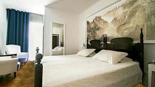 Seng med udskåret hovedgærde i et rum med vægspejl og siddepladser. (AI-genereret tekst)