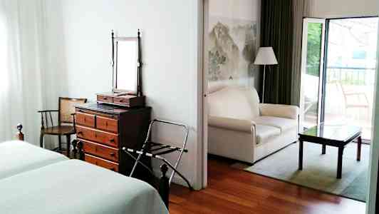 Et hotelværelse med to senge, en kommode med spejl og et åbent siddeområde med sofa og bord. (AI-genereret tekst)