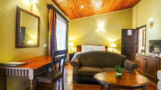 Et værelse med seng, sofa, bord, skrivebord og dekorationer. (AI-genereret tekst)