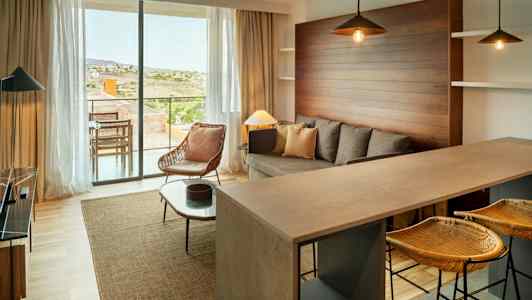 En moderne stue med sofa, lænestol og køkkenbar. Store vinduer vender ud mod en terrasse. (AI-genereret tekst)