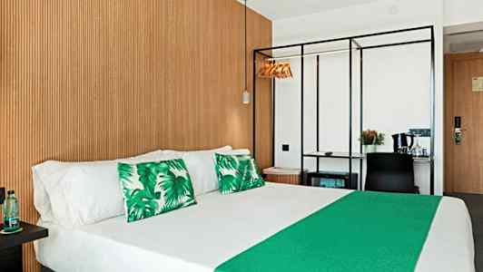 Hotelværelse med dobbeltseng, grønne pyntepuder og træpanel på væggen. (AI-genereret tekst)