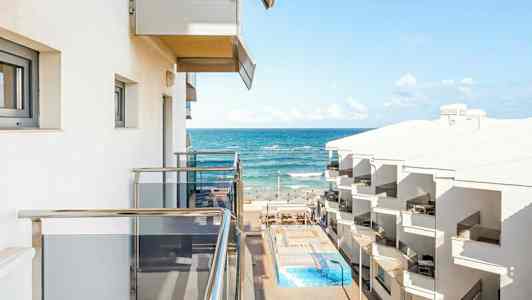 Udsigt fra altan mod havet med hotelbygninger og pool. (AI-genereret tekst)