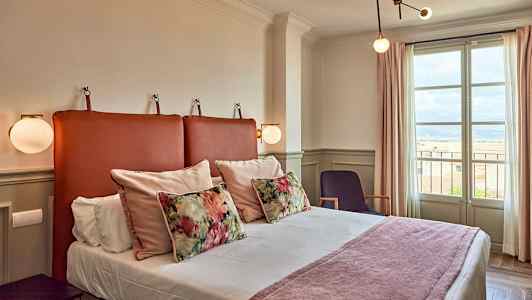 Et hotelværelse med en seng, dekorative puder og et vindue med udsigt. (AI-genereret tekst)