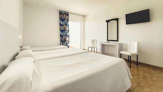 Et hotelværelse med tre enkeltsenge, et skrivebord med spejl, to stole og et vægmonteret TV. (AI-genereret tekst)