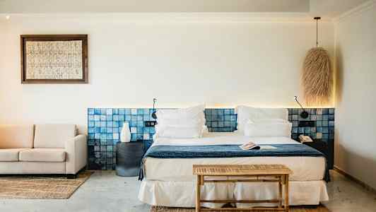 Et stilfuldt hotelværelse med en dobbeltseng, blå sengegavl, siddegruppe og lyse dekorative elementer. (AI-genereret tekst)