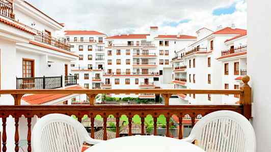 Udsigt fra en altan mod en bygning med hvide facader og røde tage. (AI-genereret tekst)